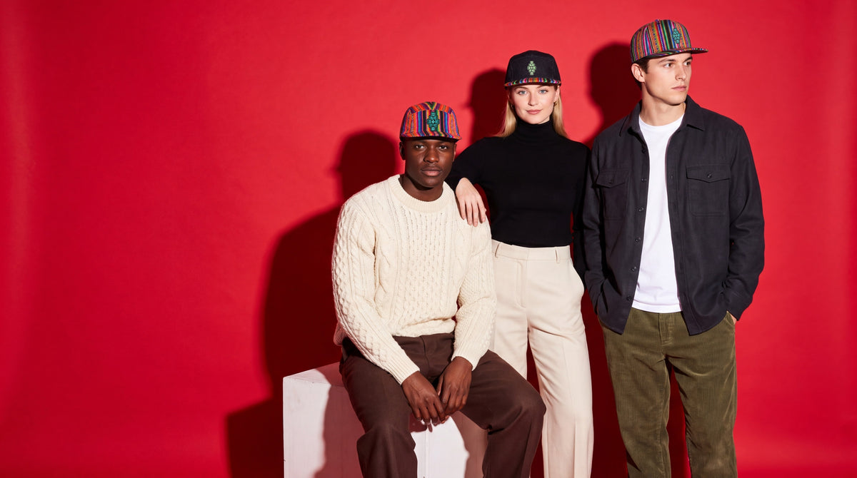 One of One — three friends in handwoven caps against a scarlet studio backdrop